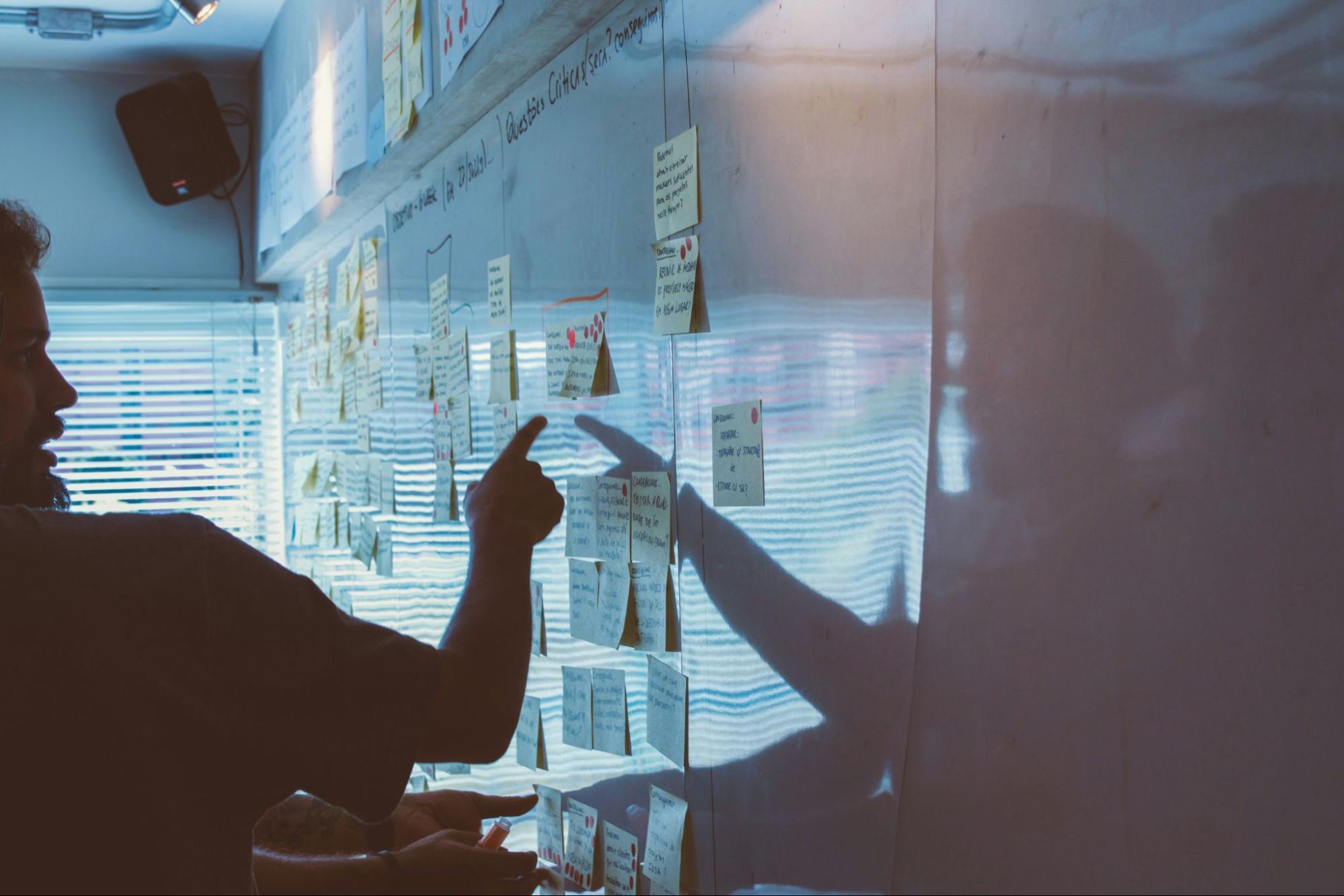 men pointing at whiteboard with post it notes in business strategy session