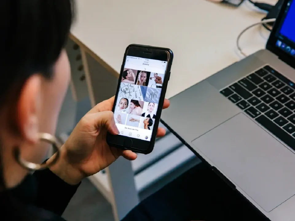 Woman viewing an Instagram profile featuring beauty and skincare content while seated next to a laptop